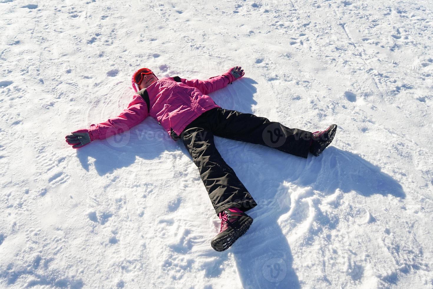 liten flicka gör en snöängel som bär snökläder foto