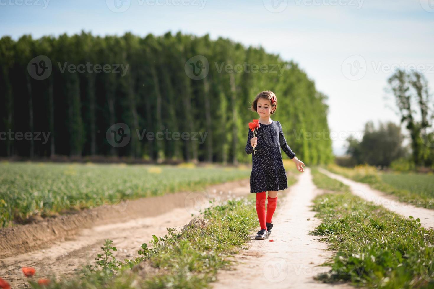 liten flicka går i naturfältet bär vacker klänning foto