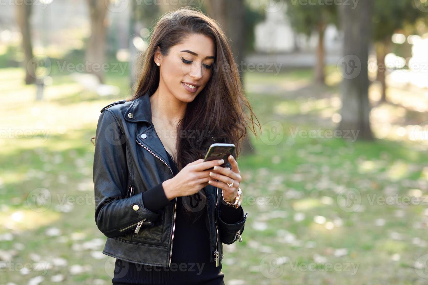 ung kvinna som använder en smartphone i en stadspark foto