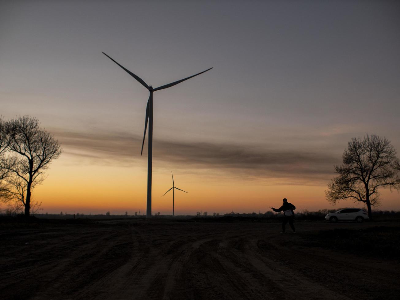 silhuetten av en man går till solnedgången i riktning mot vindkraftverk foto