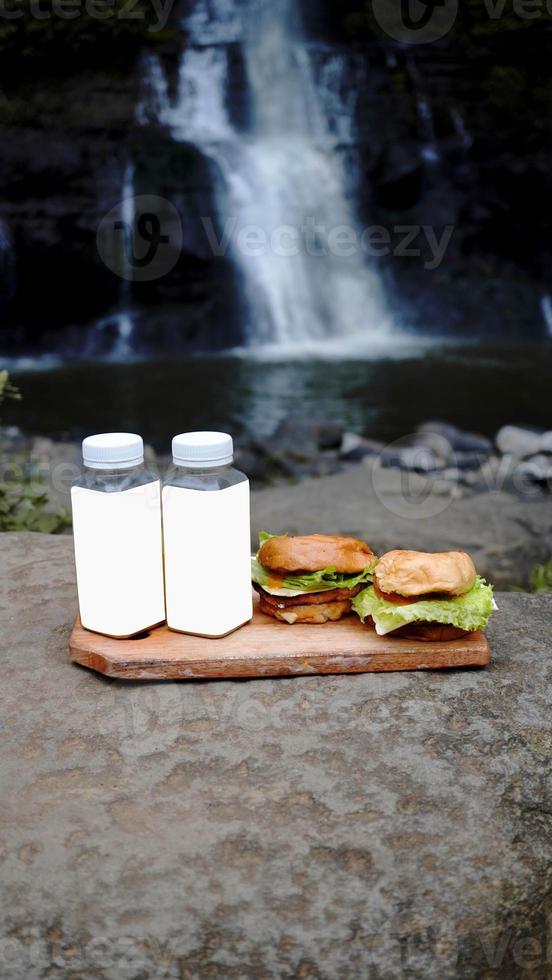 två hamburgare och två flaskor drinkar på kanten av vattenfallet foto