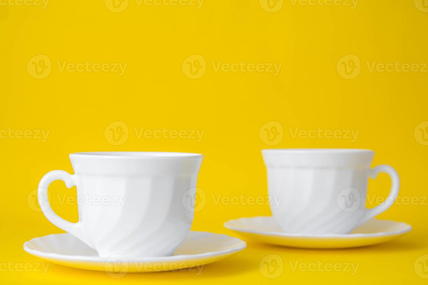 vita keramiska koppar med fat på gul bakgrund foto