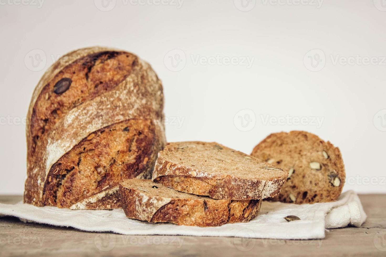 brunt färskt bröd med frön skärs i bitar på gammal träbakgrund foto