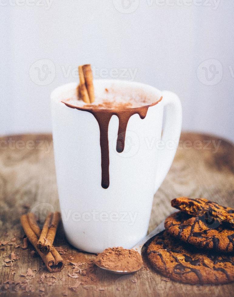 vit kopp kaffe choklad cappuccino latte med kanelstänger och chokladkakor på träbakgrund foto