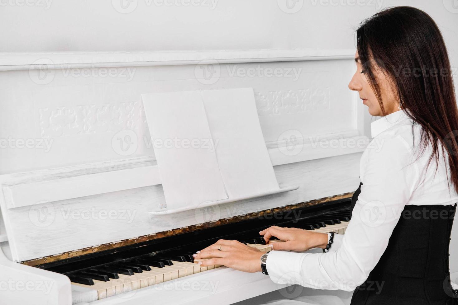 vacker kvinna klädd i vit klänning spelar på vitt piano foto