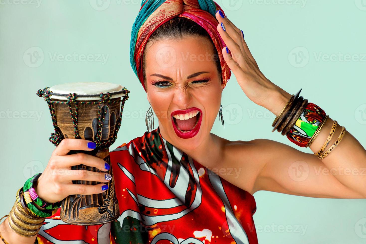 porträtt av skrikande ung attraktiv kvinna sångerska i afrikansk stil med trumma på färgglad bakgrund foto