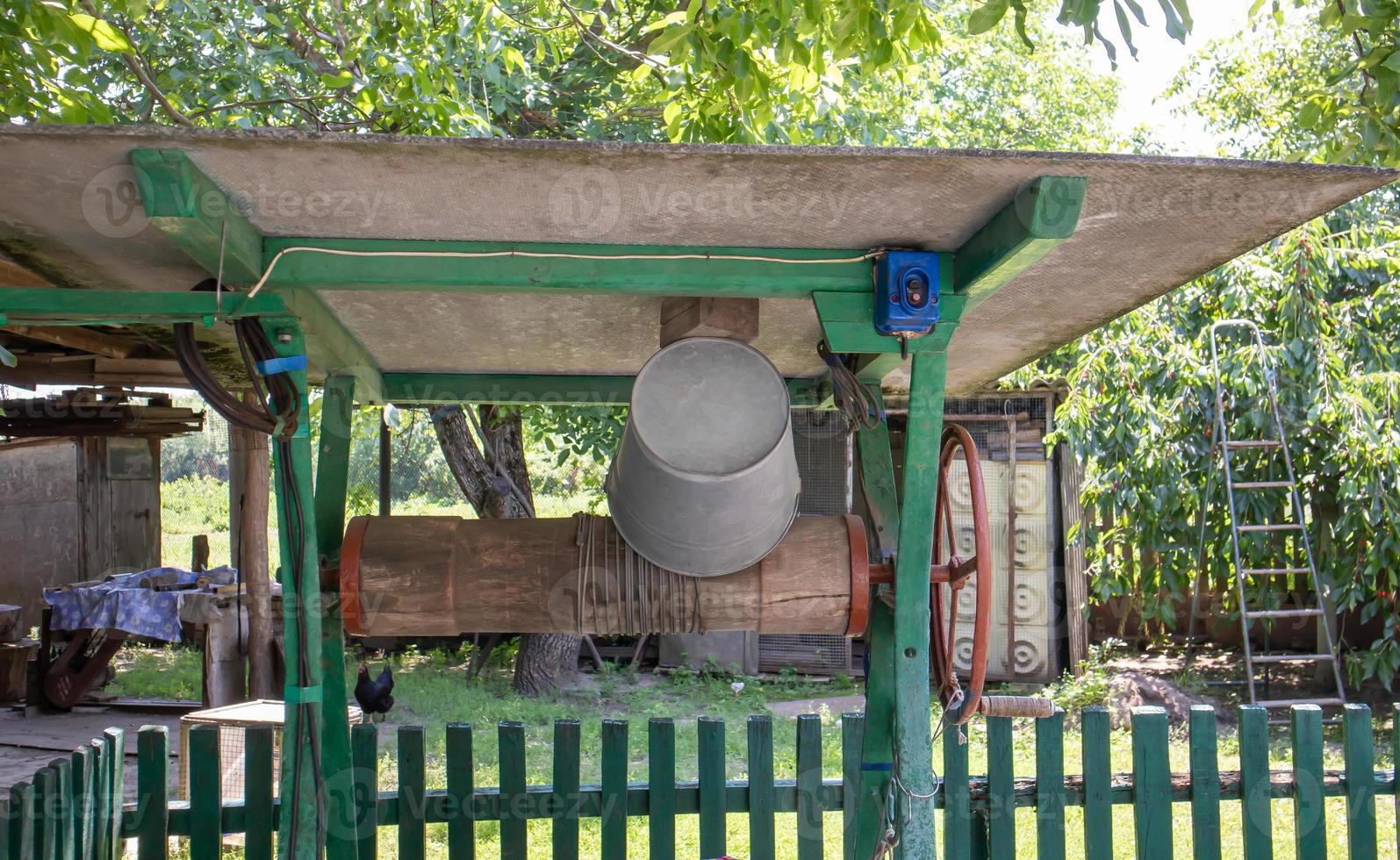 en gammal vattenbrunn med en hink i trädgården, ett metallhandtag för att lyfta vatten från marken. bybrunn under taket med ett rep. retro bra på landet. foto