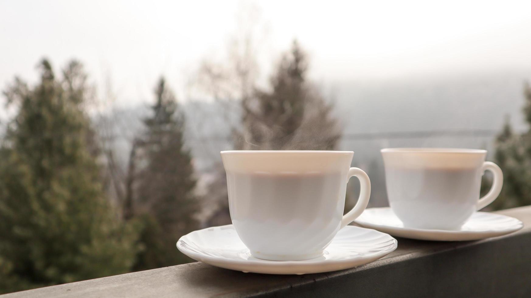 två kaffekoppar på en balkong med bergslandskap på morgonen. två koppar morgonkaffe, stående vid sidan av balkongen, med en magisk utsikt över höstens skogar. foto