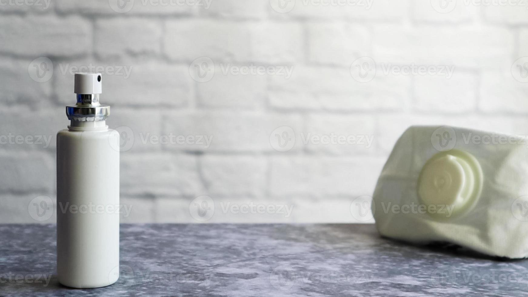 vit antiseptisk flaska och en mask av en skyddande medicin på ett grått bord, på en bakgrund av en vit tegelvägg. förebyggande av coronavirus sjukdom covid-19 under ett utbrott av influensavirus foto