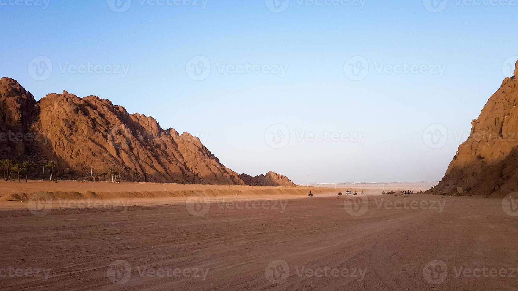 öknen i egypten. steniga sandkullar. en ensam turist på en atv i öknen mot bakgrund av blå himmel och berg går mot röda havet. landskap i öknen. foto