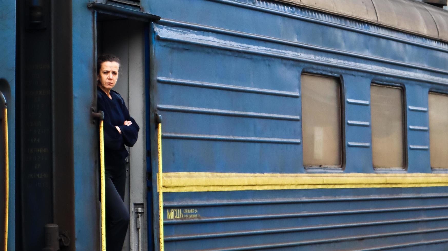 ukraina, yaremche - 20 november 2020. en tågkonduktör, en kvinna med europeiskt utseende, i mörkblå uniformer, står vid dörren till en passagerarvagn och väntar på avgång. utsikt över järnvägen. foto
