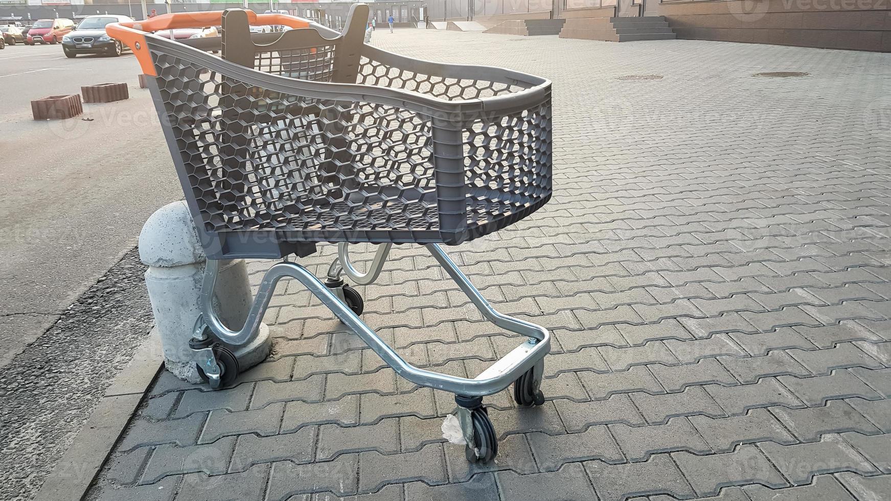 tom livsmedelsbutik utomhus nära snabbköpet. ensamhet, vagnisolering, karantän, coronavirus. en tom plastkorg på hjul med gula plastdelar kvar på trottoaren nära butiken. foto