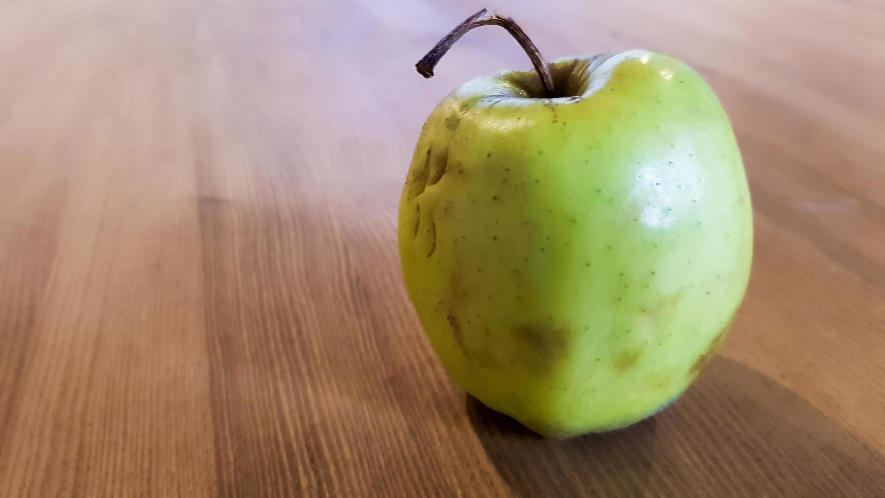 grönt ruttet äpple på en trä bakgrund. grönt äpple på en gammal trä bakgrund, ovanifrån. ekologiskt saftigt bio äpple fult, med defekter ätbara ligger på ett träbord. ingen ful mat foto