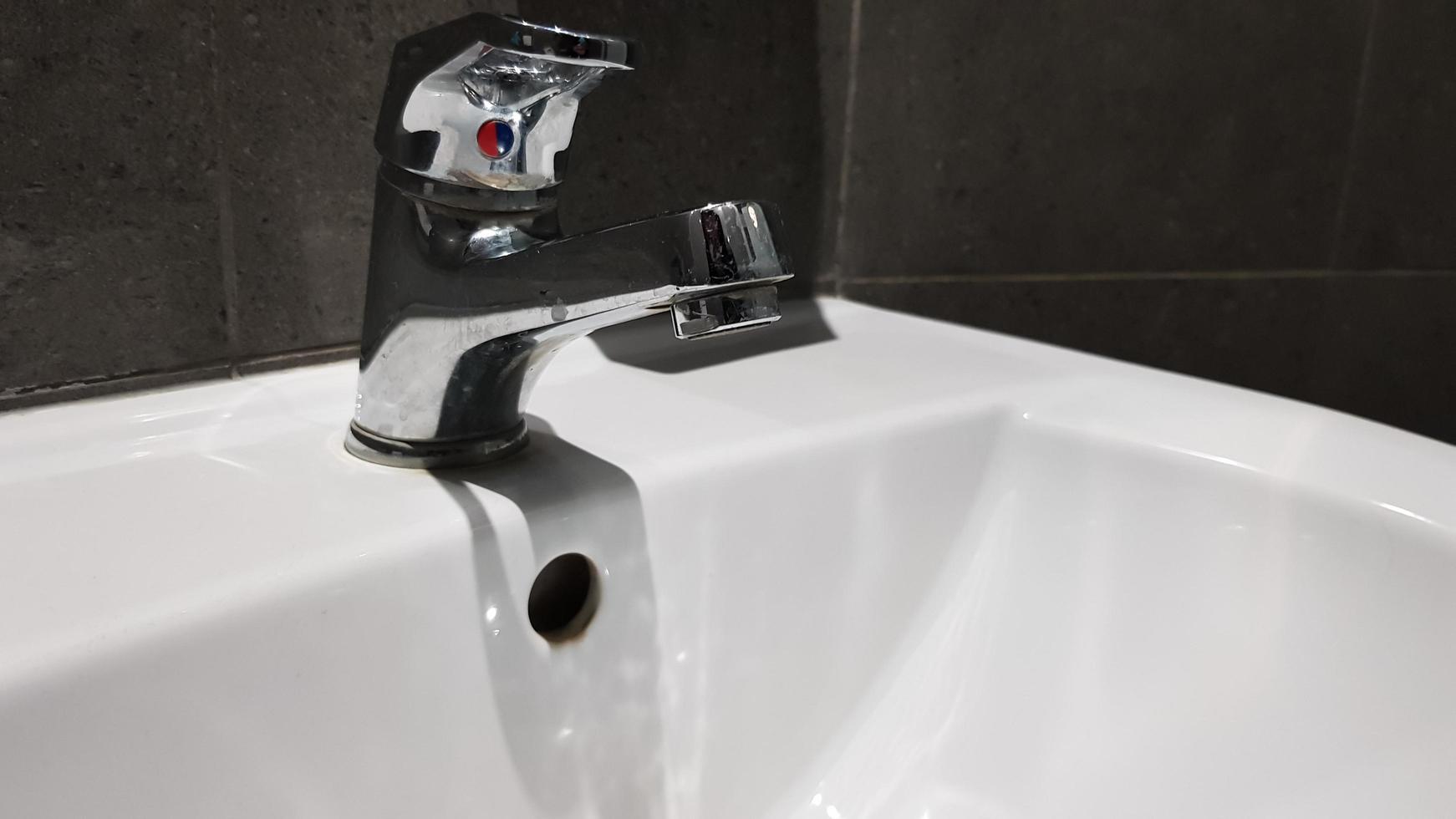 vitt keramiskt tvättställ med kromblandare på toaletten med grått kakel foto