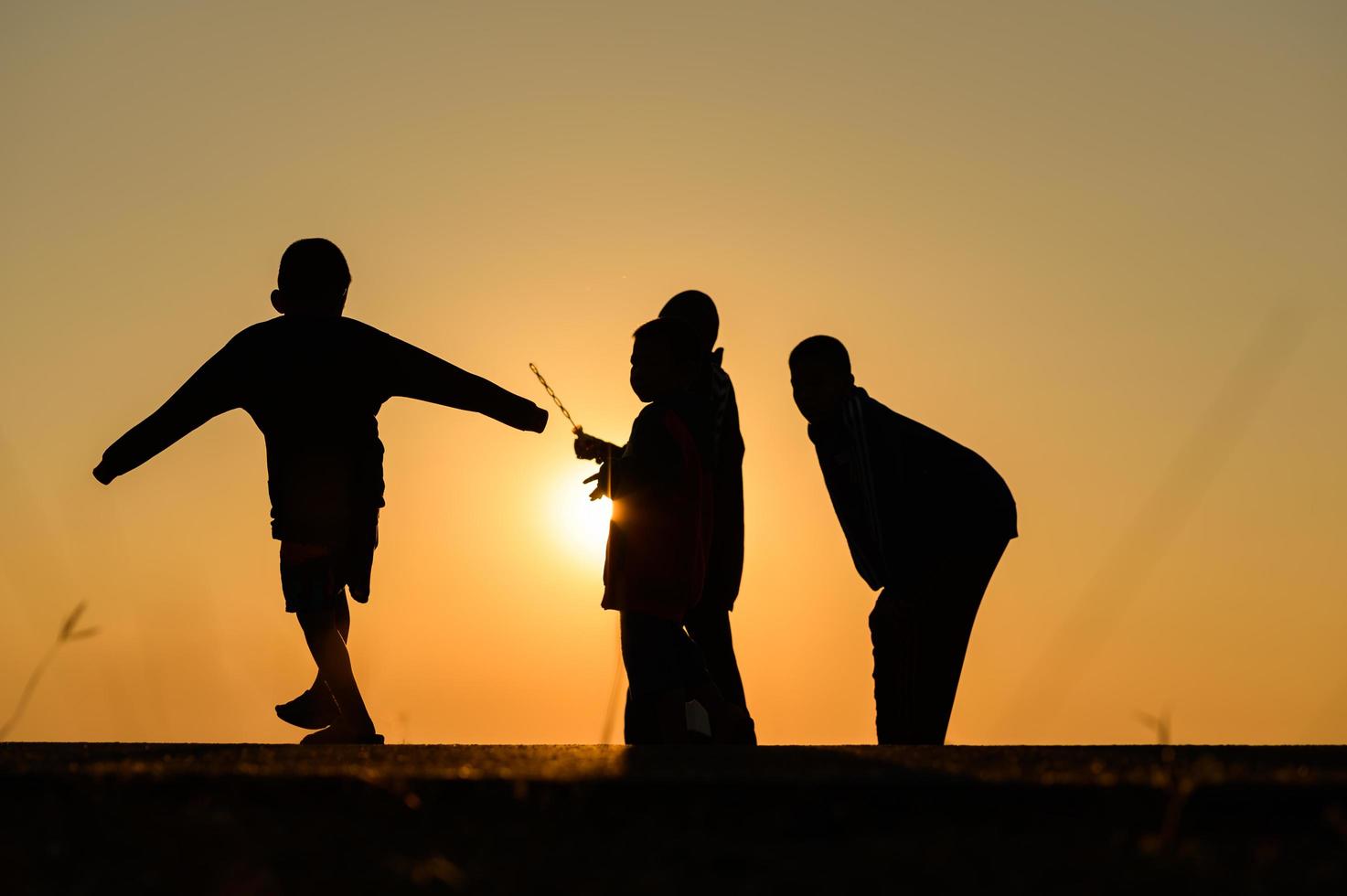 barn siluett leker kul med många vänner och spelar mot solnedgången foto