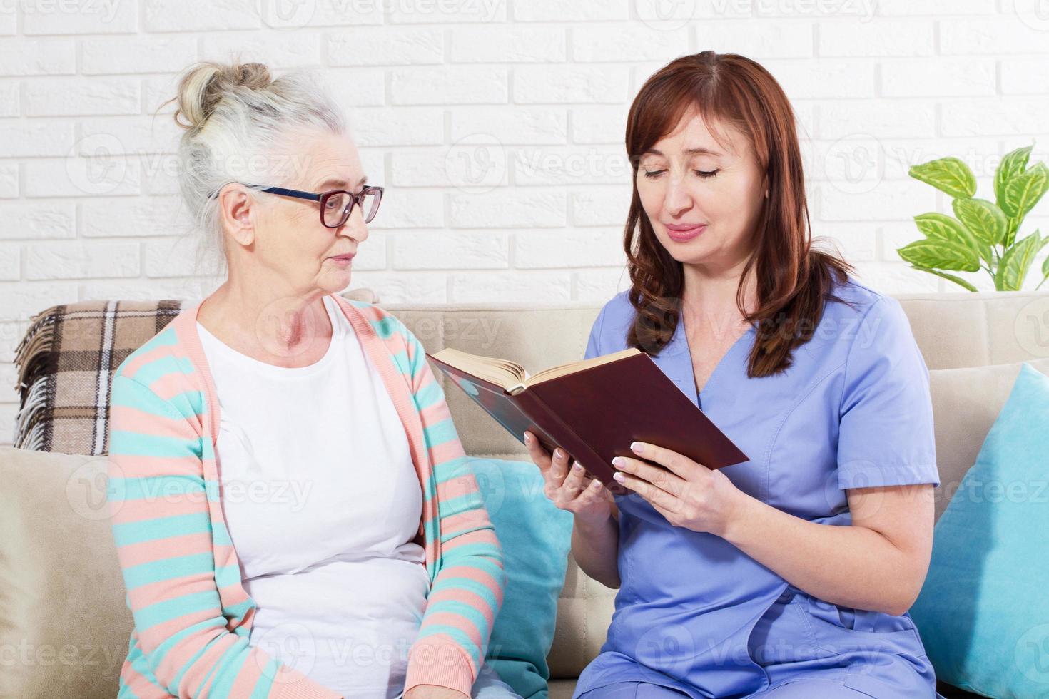 kvinna som läser en bok för en äldre kvinna på vårdhem foto
