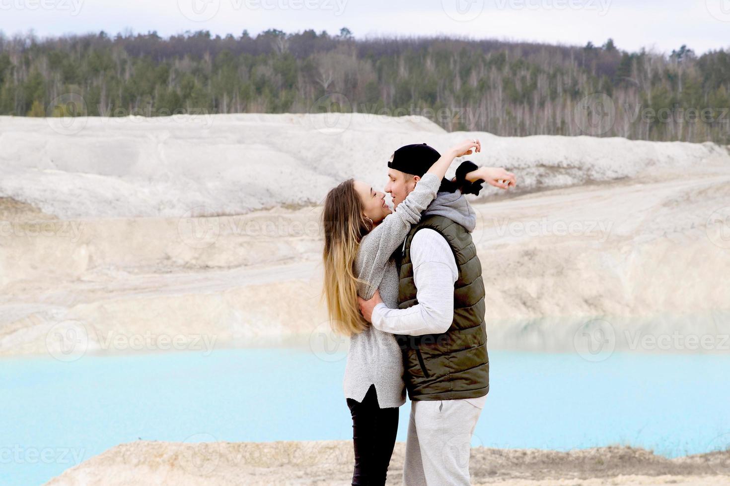 lyckligt par kramar och tittar på varandra på bakgrunden av blå sjö och sandiga berg foto