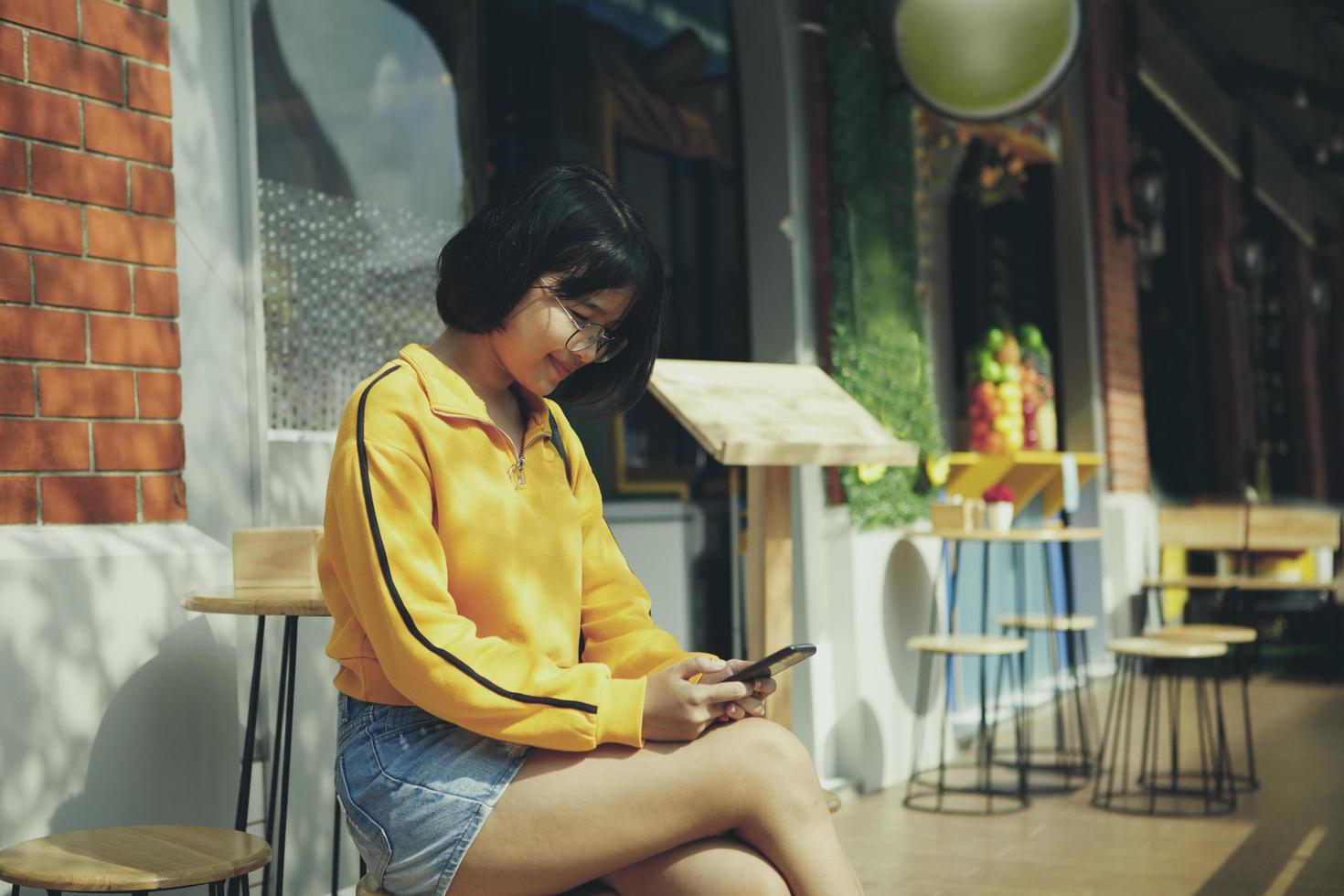 asiatisk tonåring kontrollera meddelande på mobiltelefon på city street cafe foto