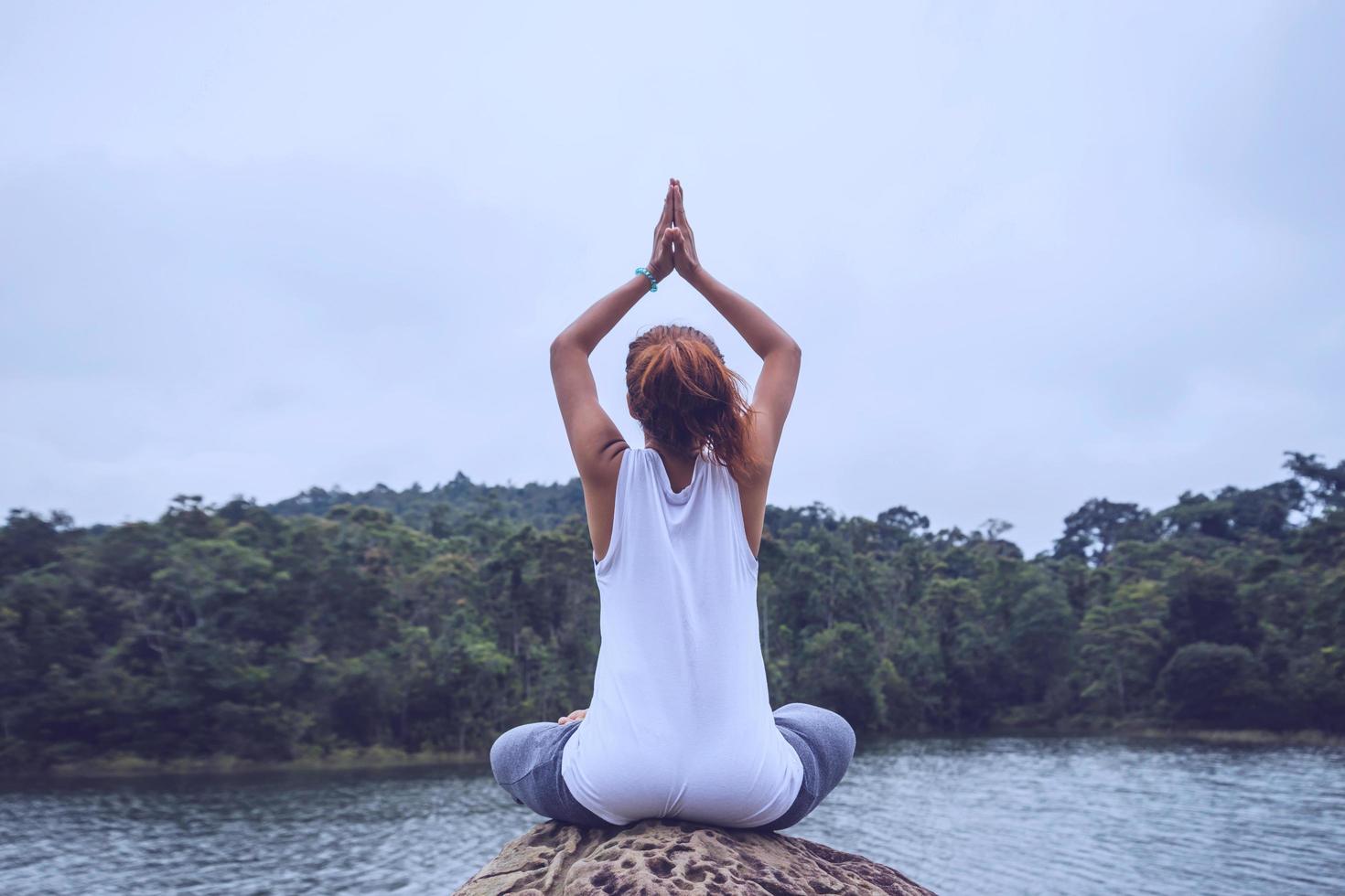 asiatiska kvinnor koppla av i semestern. spela om yoga. på klipporna mitt i vattnet. foto