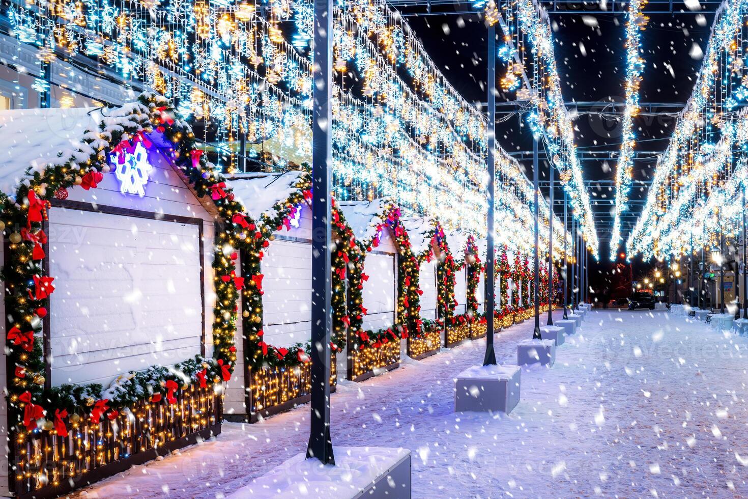 jul eller ny år marknadsföra i en europeisk stad med hus dekorerad med kransar på natt i snöfall. foto