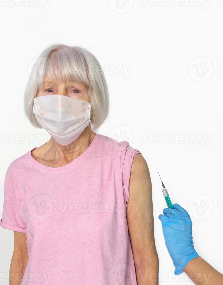 rädd senior kvinna i mask och läkares händer i medicinska handskar med spruta under vaccination på vit bakgrund. hälsovård, vaccination koncept foto
