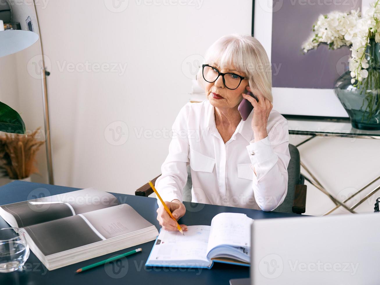 trött senior vacker grått hår kvinna i vit blus som arbetar på laptop på kontoret. arbete, seniorer, frågor, hitta en lösning, uppleva koncept foto