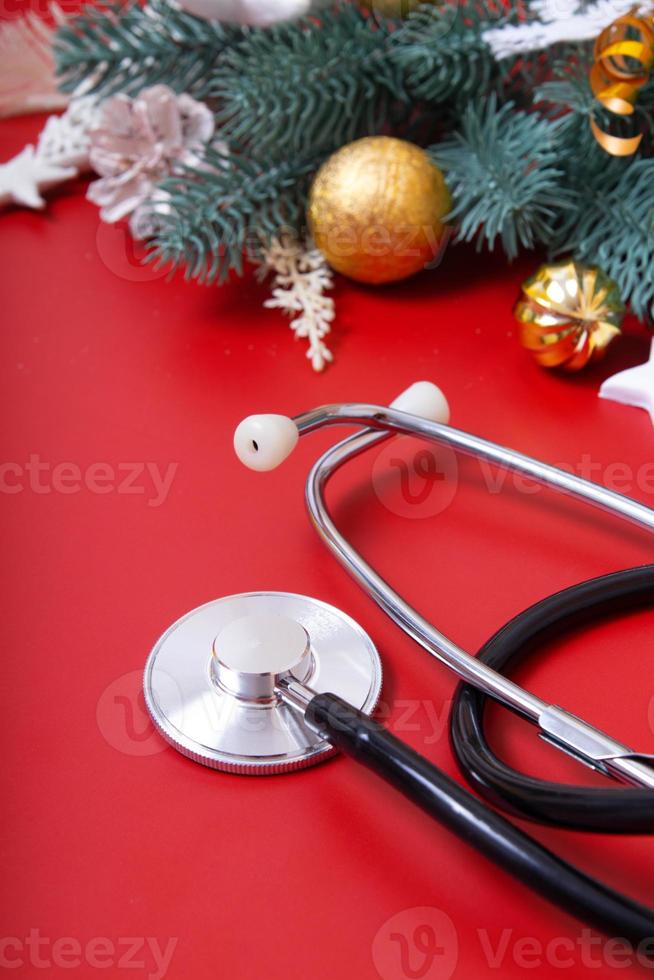 medicinskt stetoskop och juldekorationer på en röd bakgrund. jul medicinska koncept foto
