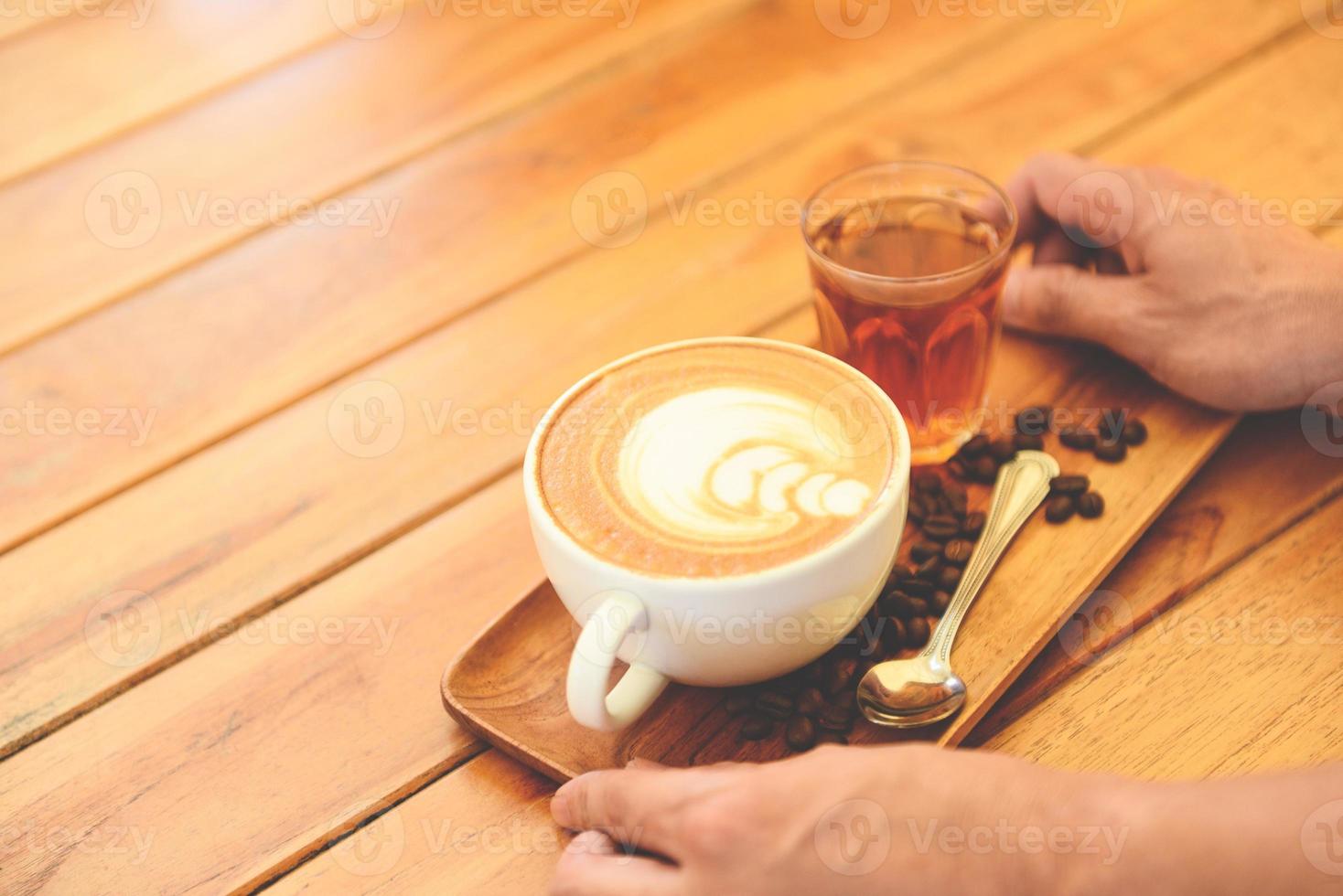 kaffekopp i handen på träbord i café med kaffebönor bakgrund, serverad kaffe cappuccino eller latte. foto