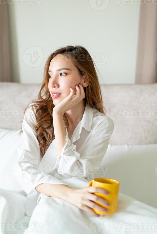 porträtt vacker kvinna vaknar och håller kaffekopp eller mugg på sängen foto