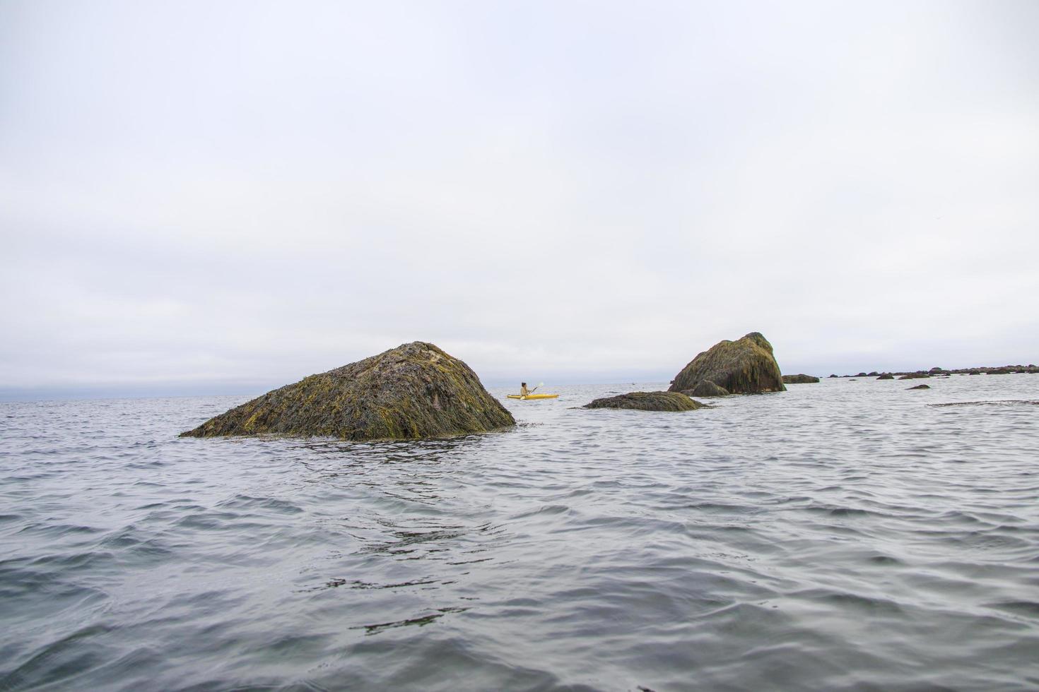 kvinna paddla kajak i en gul kajak runt stenar i havet foto