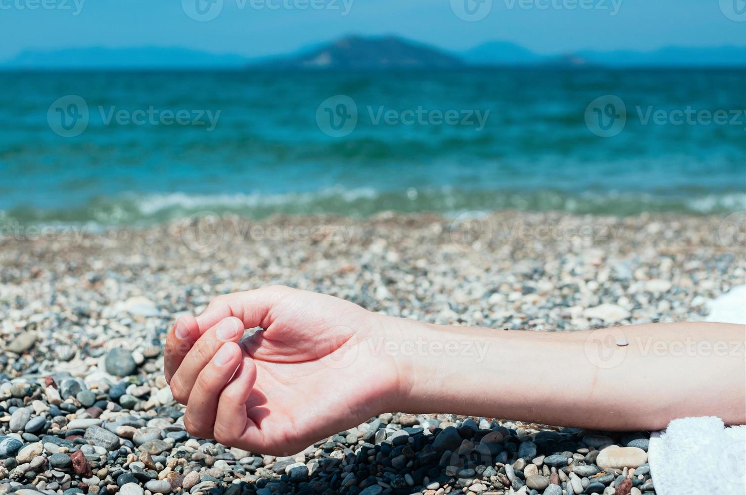 hand av en man som kopplar av på stranden, turkost havsvatten i bakgrunden foto