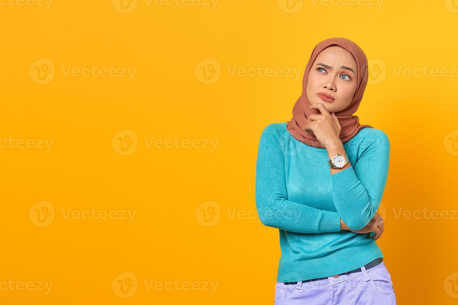 fundersam ung asiatisk kvinna tänker på något på gul bakgrund foto