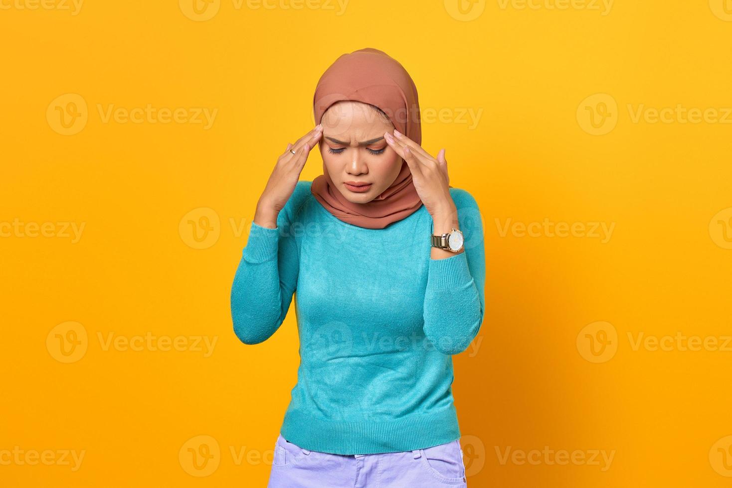 vacker ung asiatisk kvinna ser yr och har huvudvärk på gul bakgrund foto