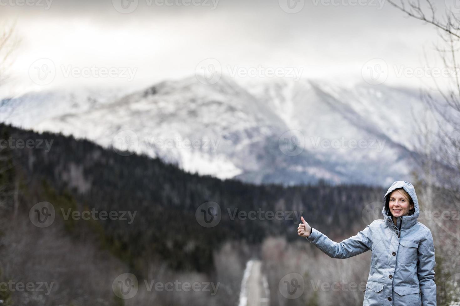 kvinna liftar på en vinterväg med vackra snöiga berg i bakgrunden foto