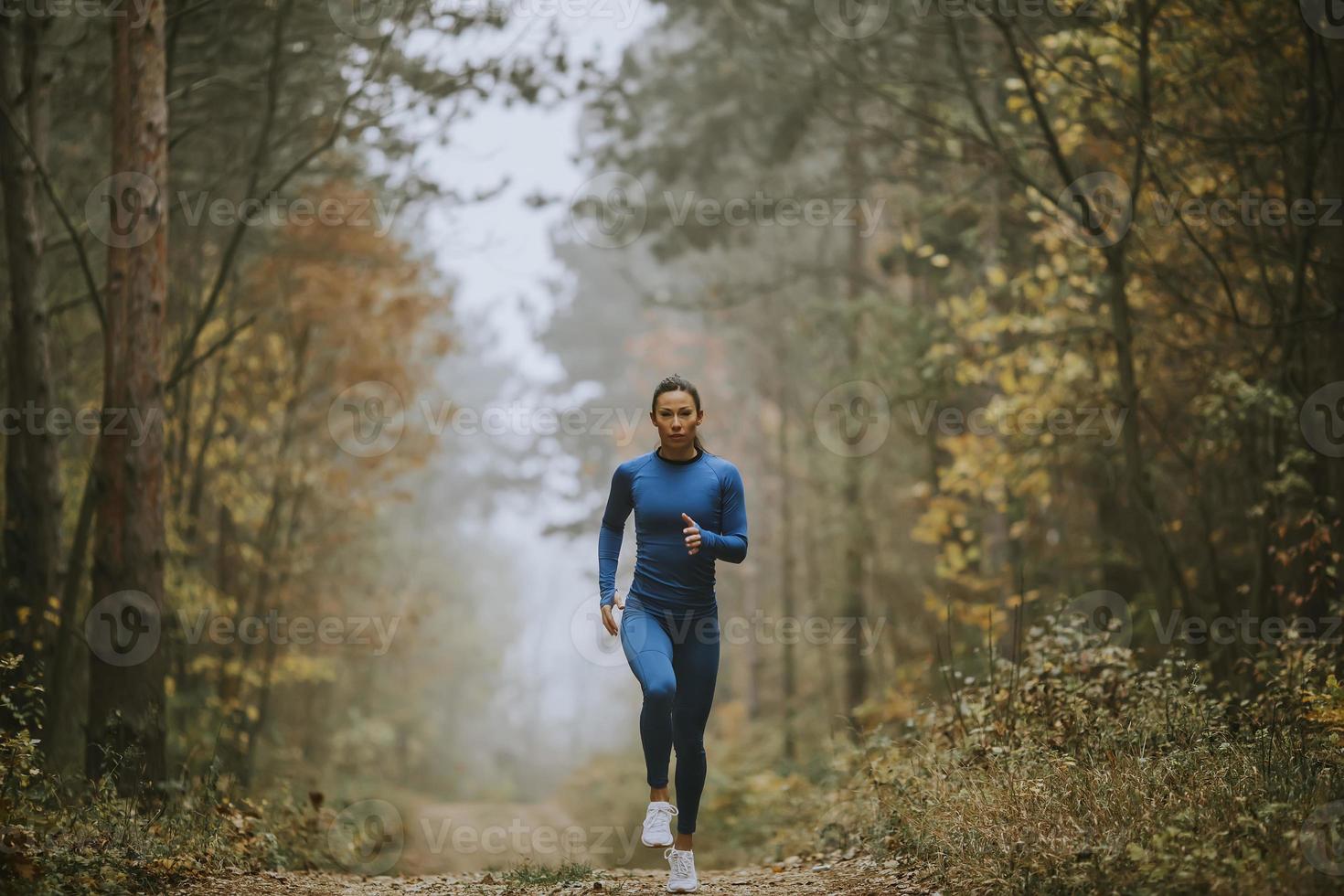 ung kvinna springer mot kameran på skogsstigen på hösten foto