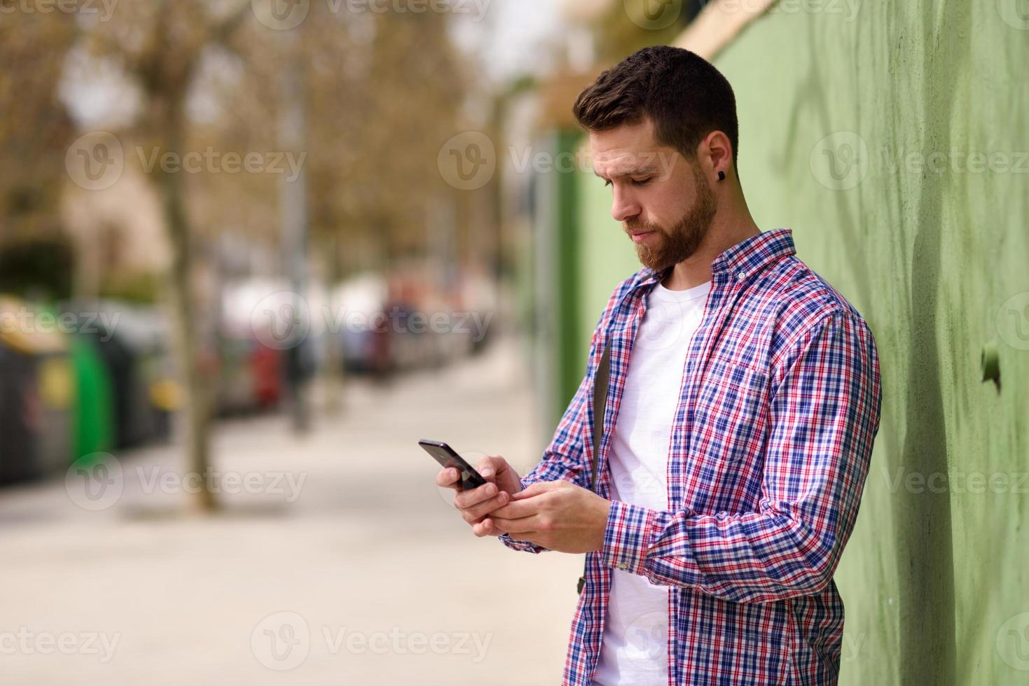 ung man ser sin smarta telefon i urban bakgrund. livsstilskoncept. foto