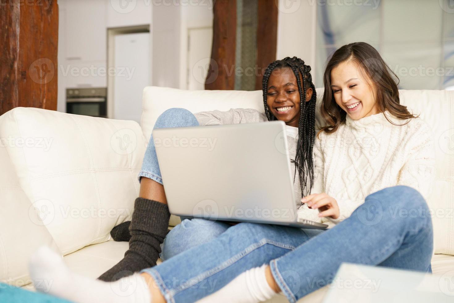 två kvinnliga studentkompisar sitter i soffan hemma med en bärbar dator. foto