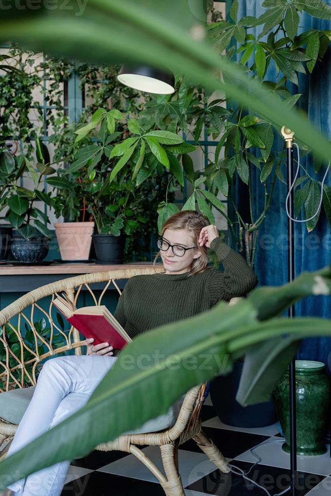 ung blond kvinna sitter i bekväm stol och läser en bok foto