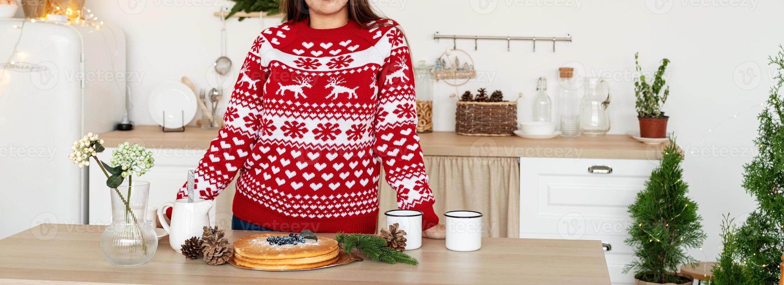 glad ung kvinna i jultröja som gör varma drycker i köket foto