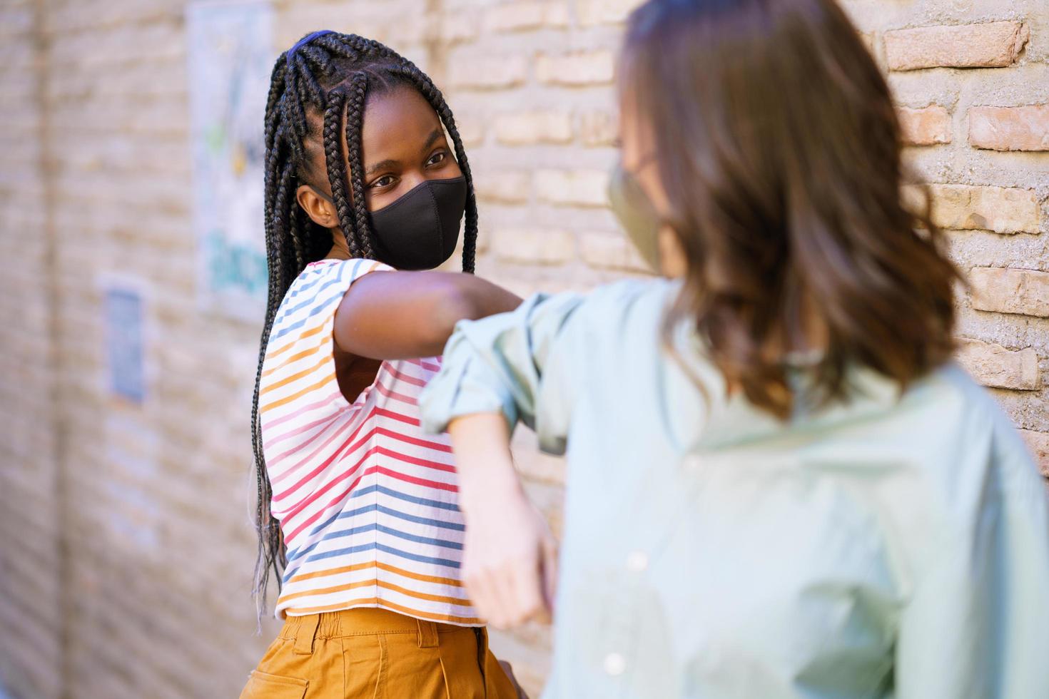 multietniska unga kvinnor som bär masker hälsar på varandra med sina armbågar foto