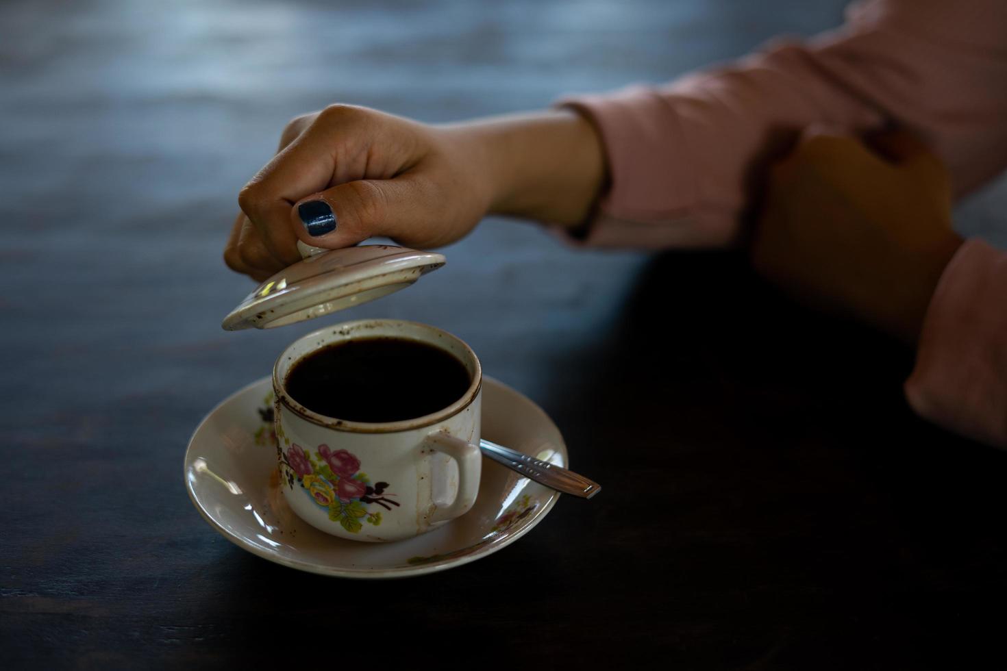 en kopp varmt kaffe står på bordet. en flicka håller en välsmakande dryck i handen. ett slags njutning av fritiden. foto