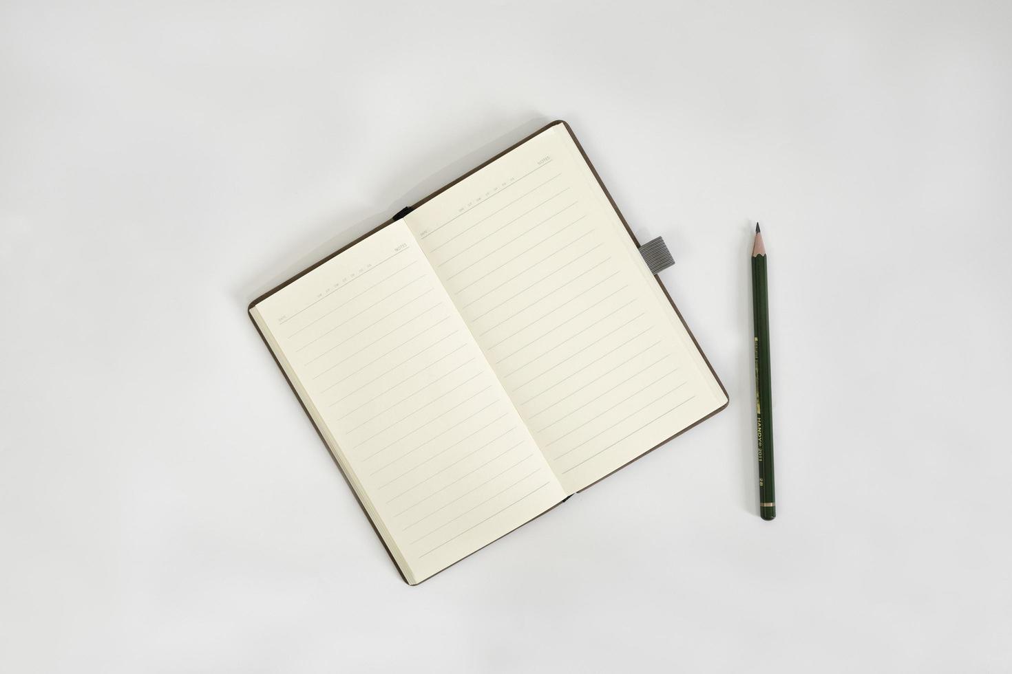 vitt skrivbord med skissbok och penna ovanpå. en anteckningsbok mockup på skrivbordet som en arbetsyta layout. kontorsobjekt isolerad på vit bakgrund. foto