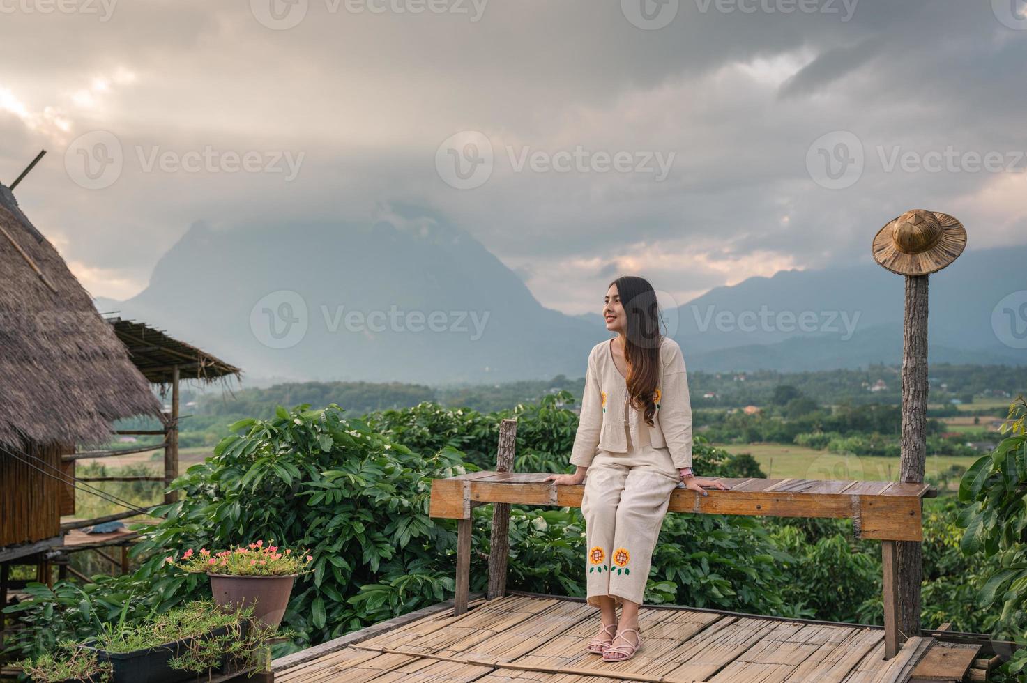 ung asiatisk kvinna sitter på terrassen och utsikt över bergen i doi luang chiang dao i solnedgången foto