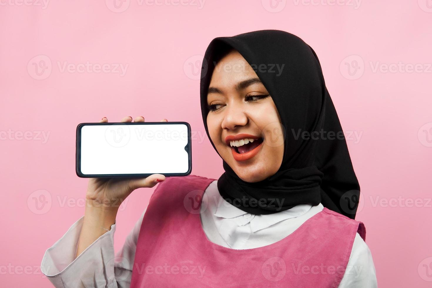 närbild av vacker och glad ung muslimsk kvinna som håller smartphone med vit eller tom skärm, marknadsför app, främjar något, isolerat, reklamkoncept foto