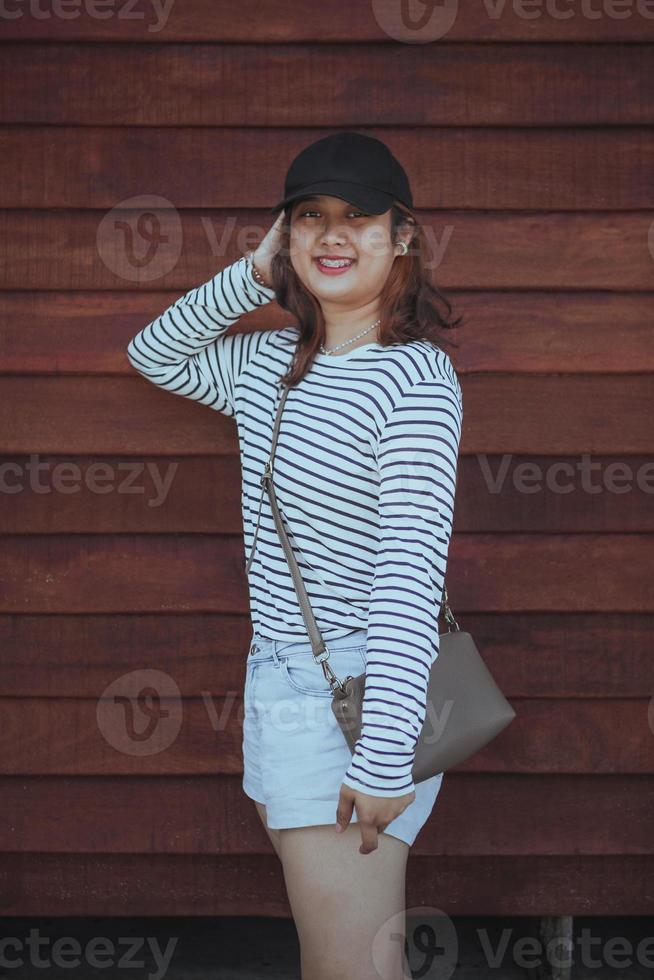 asiatisk yngre kvinna toothy leende stående mot trävägg foto