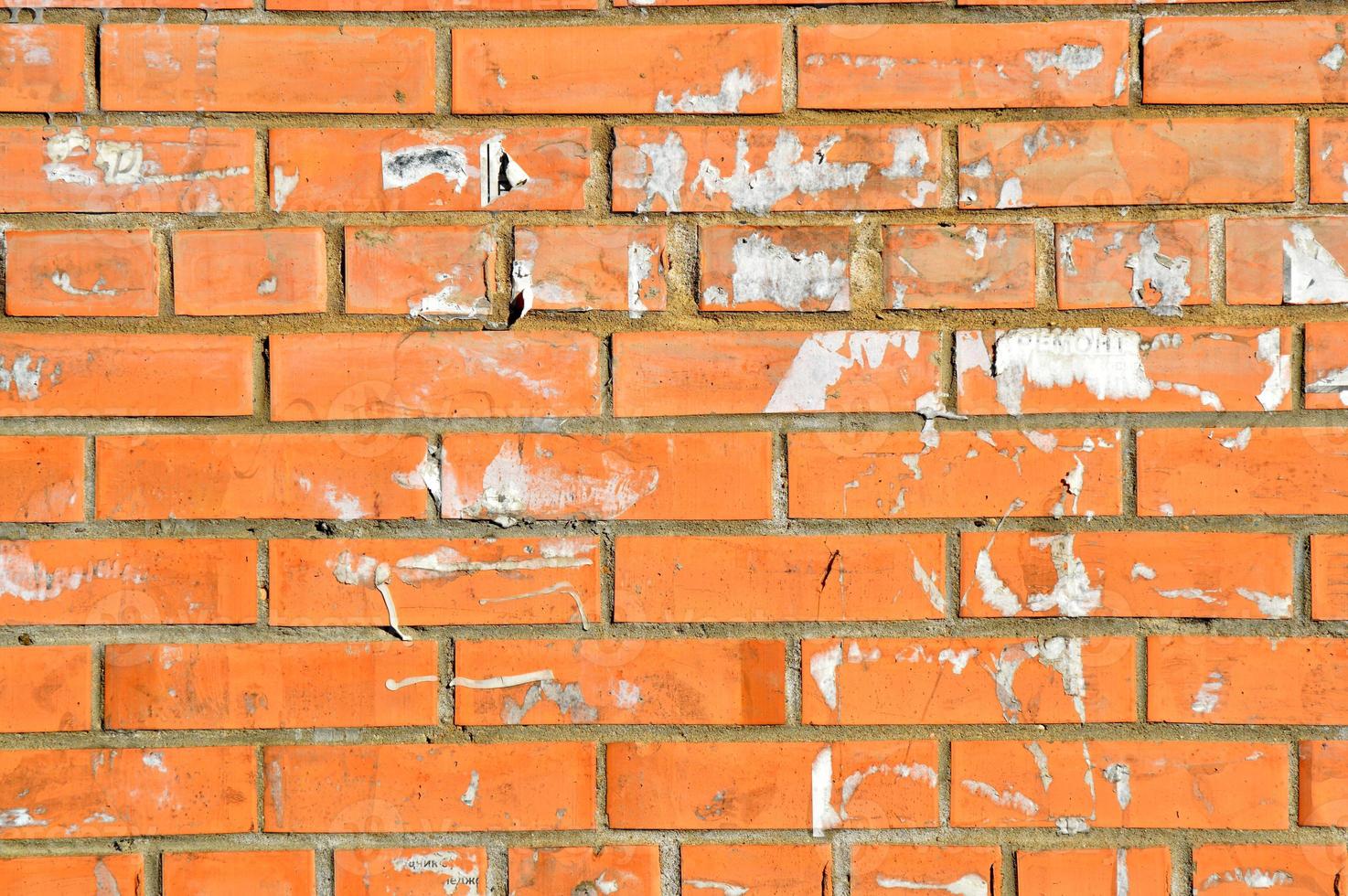 gammal orange tegelvägg. målad sliten väggyta. vintage röd tegelvägg med tecken på gamla annonser på den. urban fotobakgrund för design. byggnadsfasad med skadad puts foto