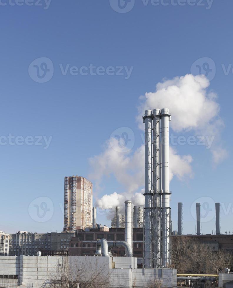 vit rök kommer från en vit skorstensvärmestationsrör på en blå himmelsbakgrund. foto