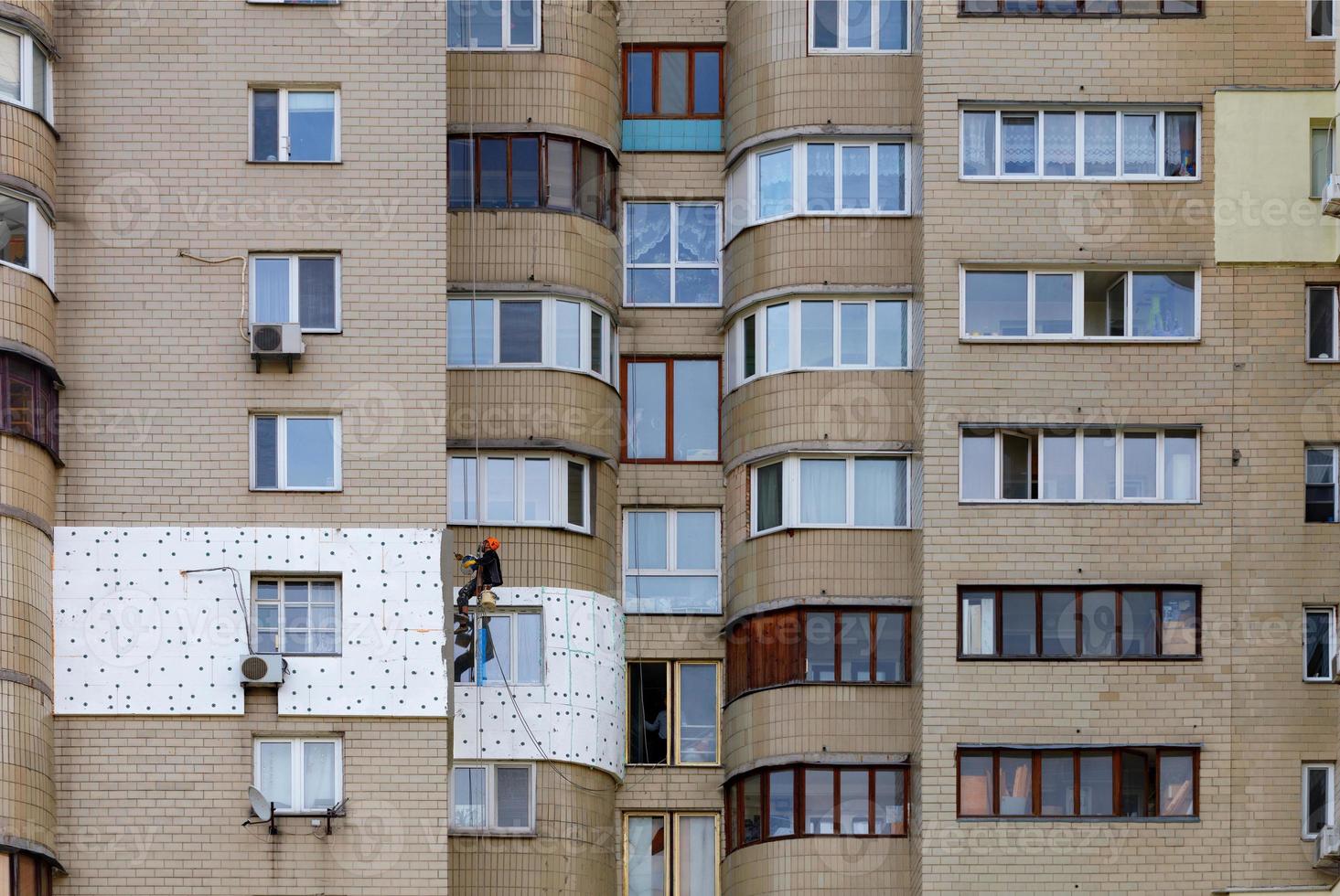 en klätterbyggare på en upphängd plattform isolerar fasaden på en separat lägenhet i ett flervåningshus med vit skumplast. foto