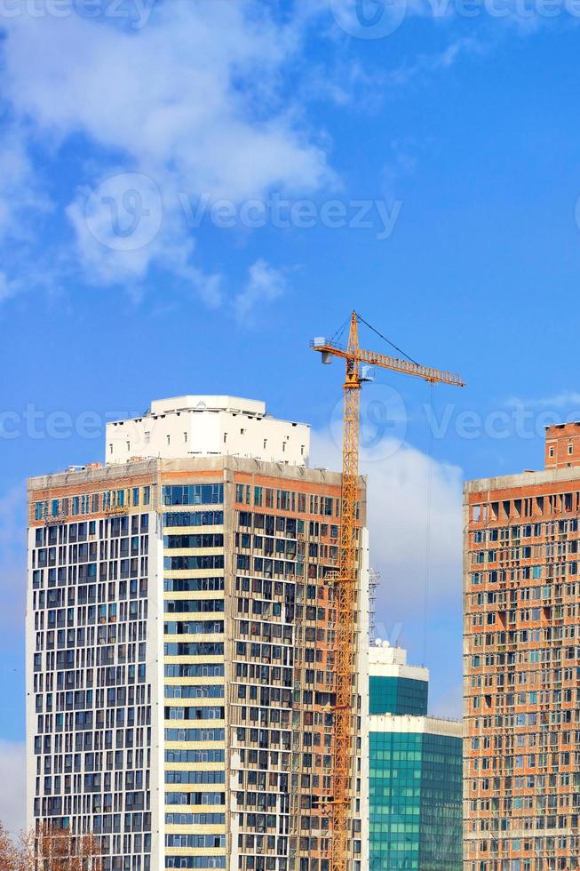 fragment av konstruktion av moderna bostadsskyskrapor med tornkran på en bakgrund av blå himmel. foto