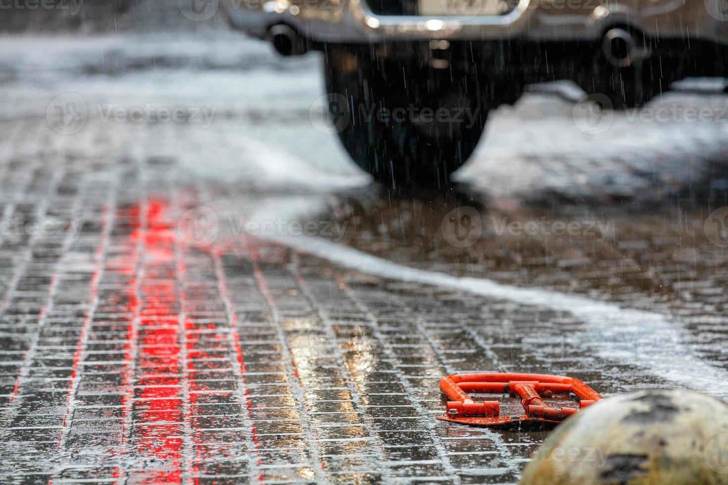 kraftigt regn sköljer de platta raderna av gatstenar på parkeringsplatsen, som reflekterar det röda ljuset från trafikljuset. foto